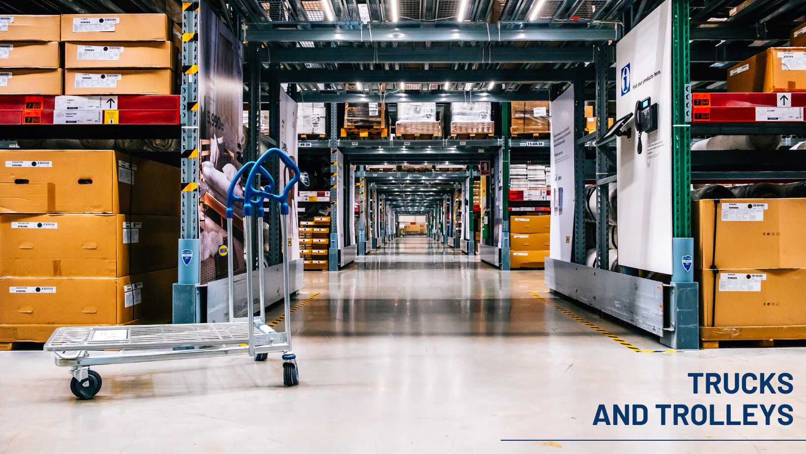 Warehouse aisle with a metal platform trolley in the foreground and stacked boxes on storage racks.